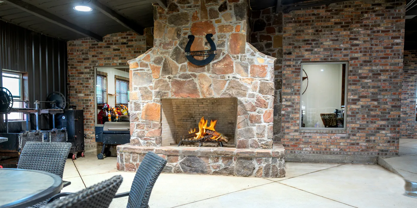 A covered lounge at Franklin Farm with a stone fireplace lit, a horseshoe above the hearth, and seating alongside.